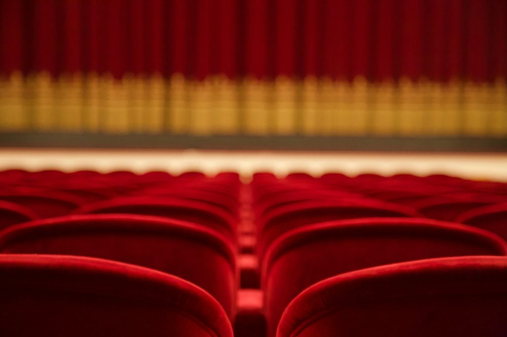 Salle de théâtre vide avec rangées de sièges rouges face à une scène
