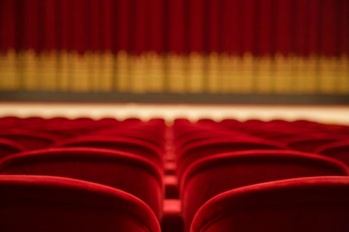 Salle de théâtre vide avec rangées de sièges rouges face à une scène