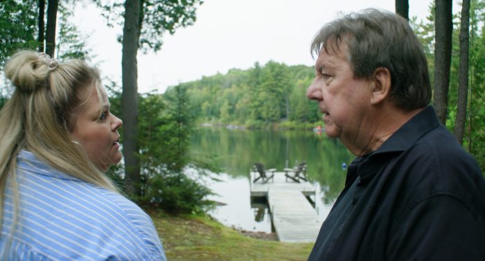 Geneviève Schmidt et Rémy Girard se regardent sur fond de lac et de forêt dans le film 125, rue des Malaises