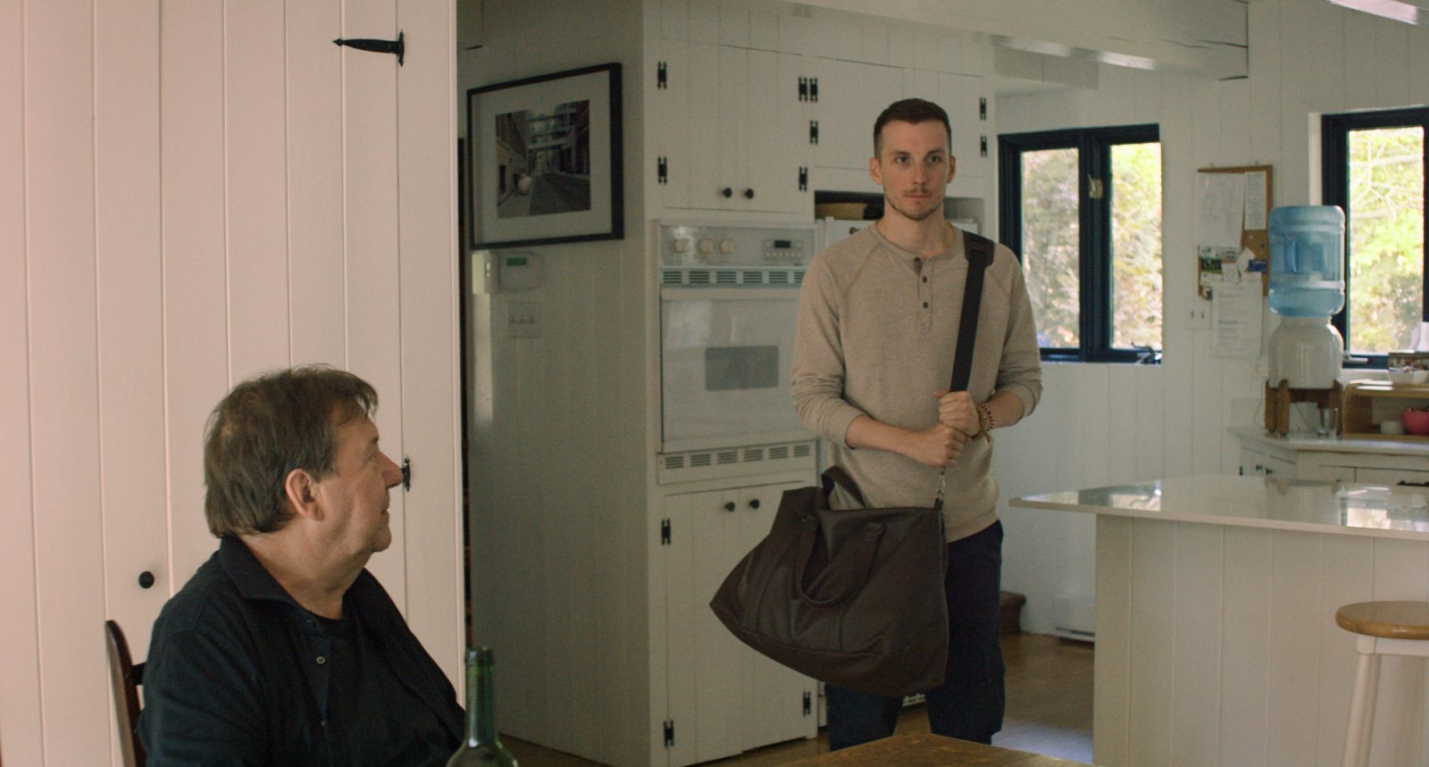 Pier-Luc Funk debout dans une cuisine et Rémy Girard assis près de lui dans une scène du film 125, rue des Malaises