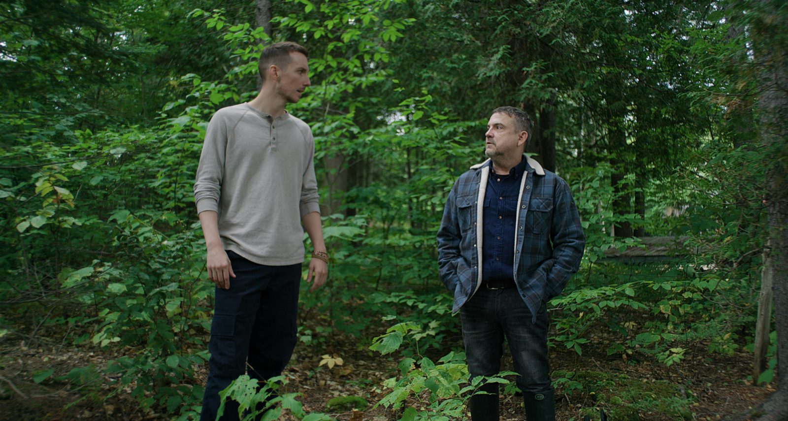 Pier-Luc Funk et Claude Legault sont debout près l'un de l'autre dans une forêt, entourés d'arbres verts, dans une scène du film 125, rue des Malaises