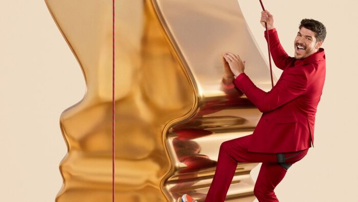 Le comédien Jason Roy Léveillée escaladant un trophée Gémeaux géant dans un habit rouge pour la promotion du 41e Gala des Prix Gémeaux qu'il anime le dimanche 13 septembre 2026.
