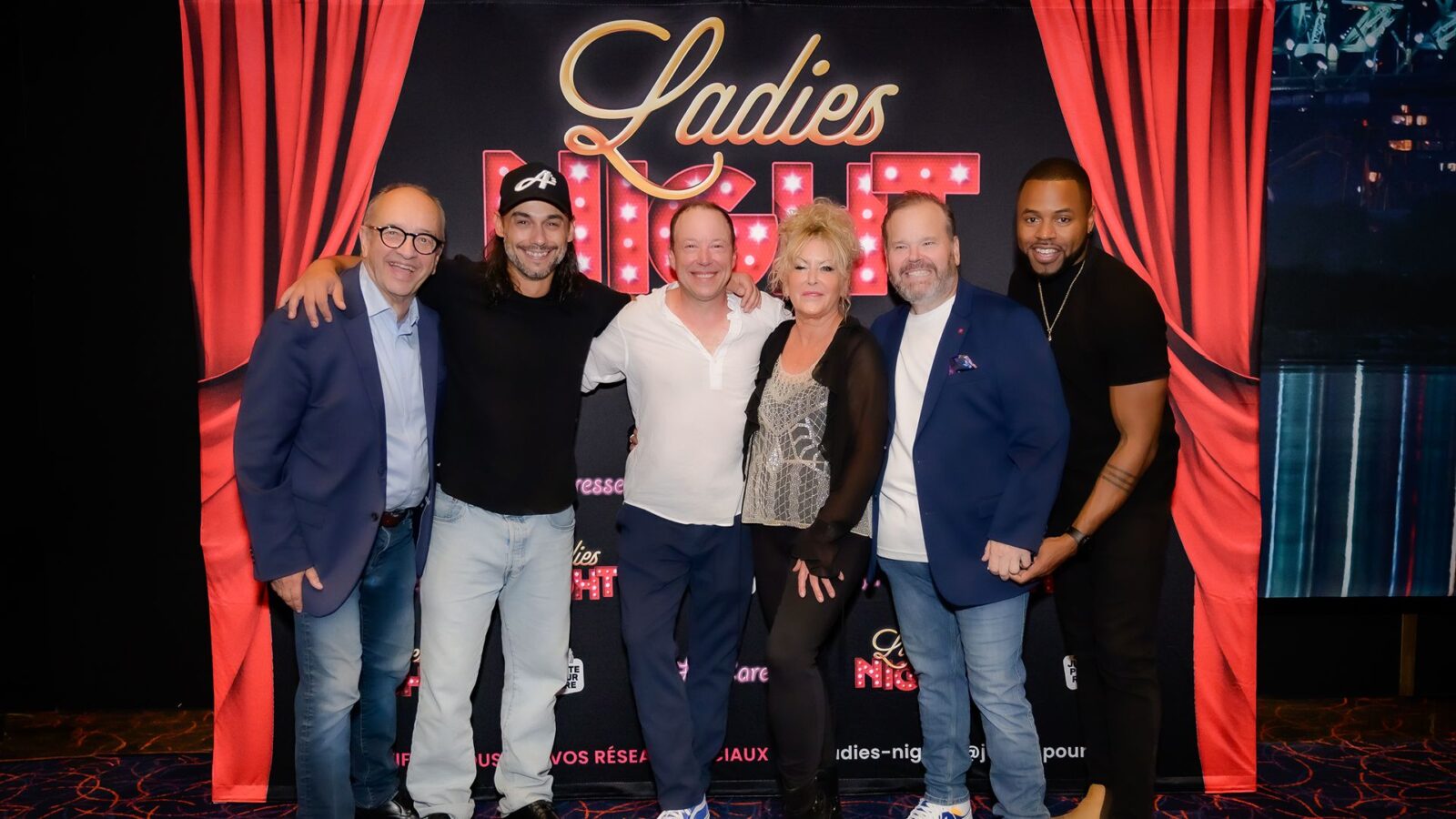 Les comédiens de la troupe Ladies Night, Marcel Leboeuf, Pierre-Paul Alain, François Chénier, Frédérike Bédard, Michel Charette et Lyndz Dantiste devant le logo beige et rouge de la pièce Ladies Night et un rideau rouge de chaque côté du groupe.