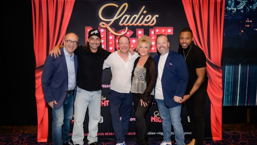 Les comédiens de la troupe Ladies Night, Marcel Leboeuf, Pierre-Paul Alain, François Chénier, Frédérike Bédard, Michel Charette et Lyndz Dantiste devant le logo beige et rouge de la pièce Ladies Night et un rideau rouge de chaque côté du groupe.